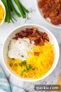 Creamy Loaded Baked Potato Dip Recipe for Parties and Game Day 10 A white bowl featuring shredded cheese, bacon, ranch, and green onions.