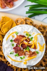 Creamy Loaded Baked Potato Dip Recipe for Parties and Game Day 12 An overhead shot of a bowl of cream dip garnished with green onion, shredded cheese, and bacon. Surrounded by corn chips and pretzels.