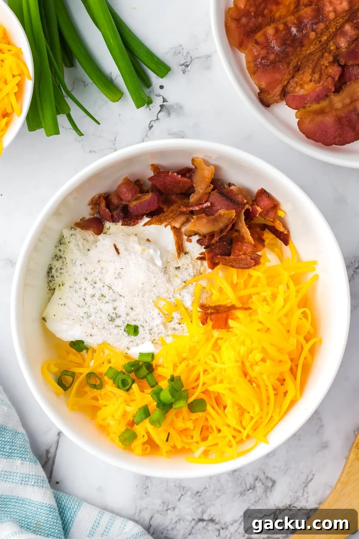 Creamy Loaded Baked Potato Dip Recipe for Parties and Game Day 4 A white bowl featuring shredded cheese, bacon, ranch, and green onions.