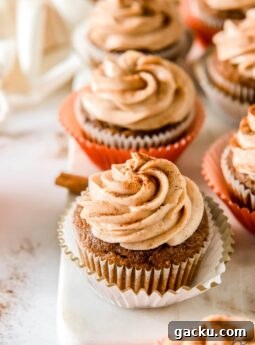 pumpkin cupcake with cream cheese frosting on open paper liner with more cupcakes behind it