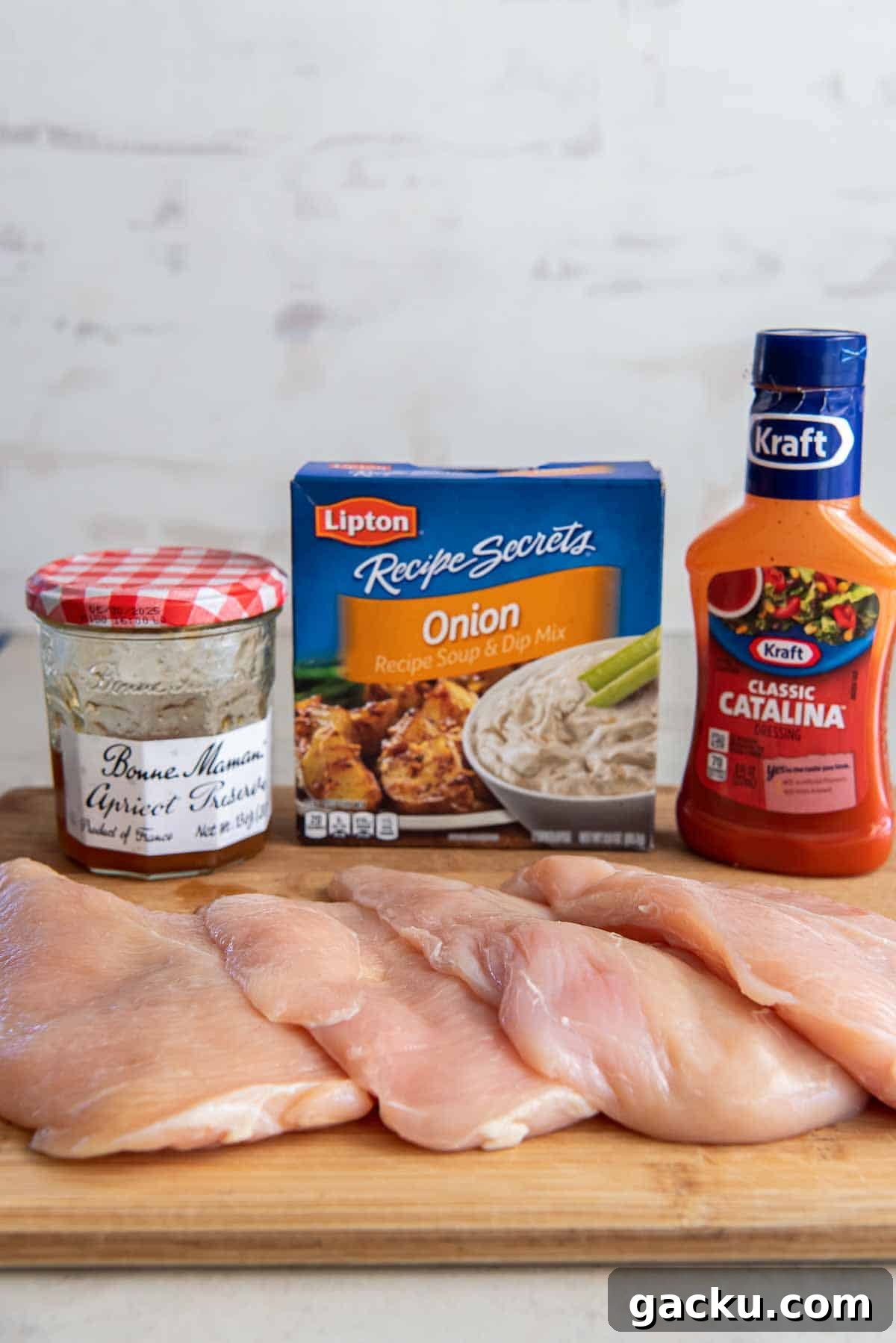 Raw chicken breasts on a cutting board with a bottle of Catalina dressing, dry onion soup mix, and apricot preserves.