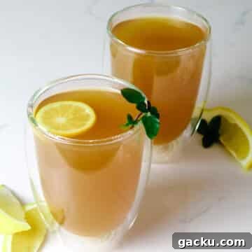 Two mugs of Honey Citrus Mint Tea with lemon slices, wedges and fresh mint.