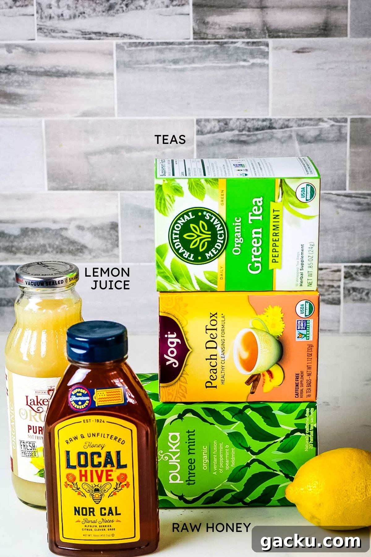 stack of three different tea boxes, fresh lemon, lemon juice in bottle and local and raw honey bottle.