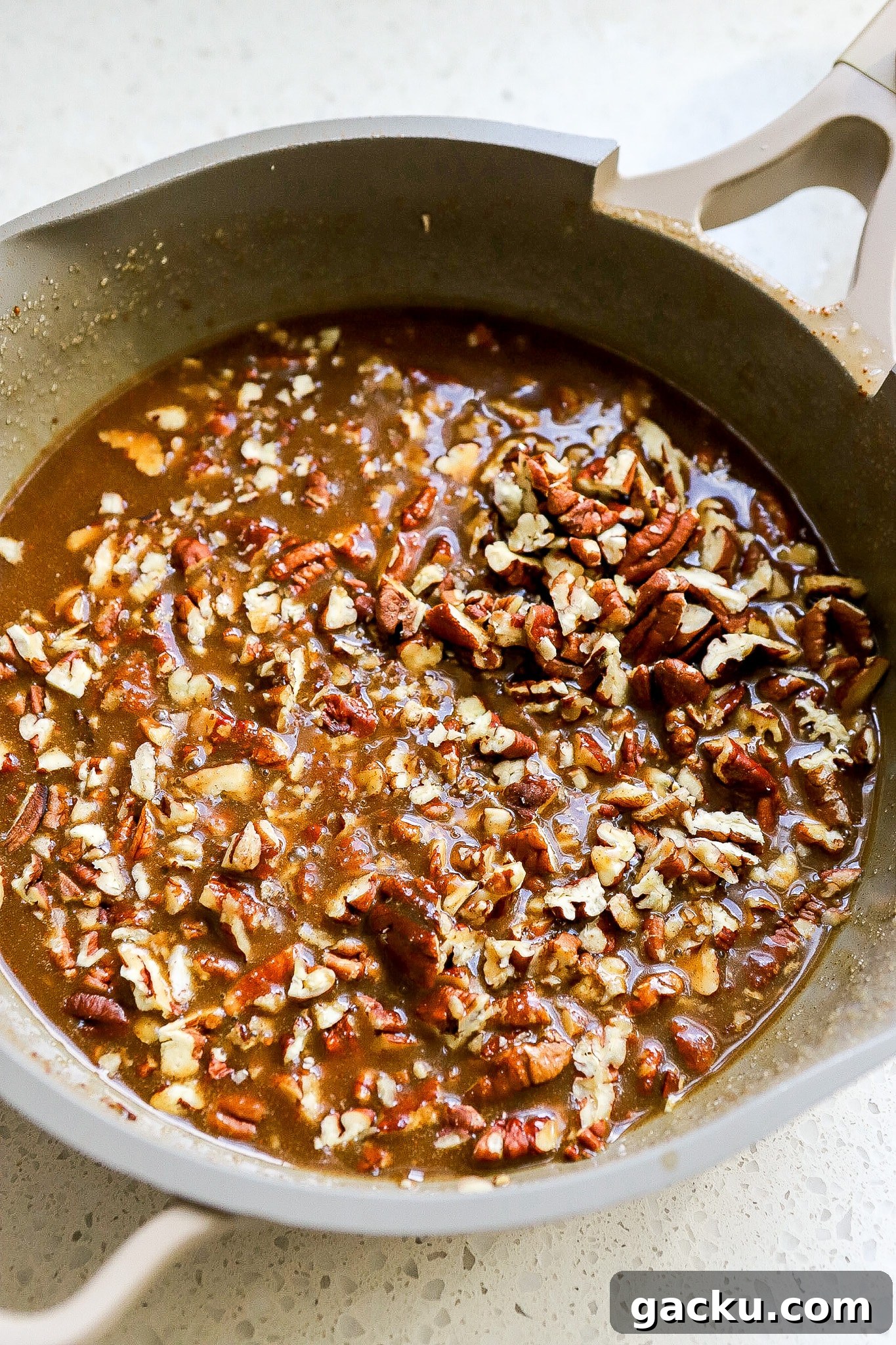 Side angle of of caramel brown sugar mixture in saucepan with pecans in it.