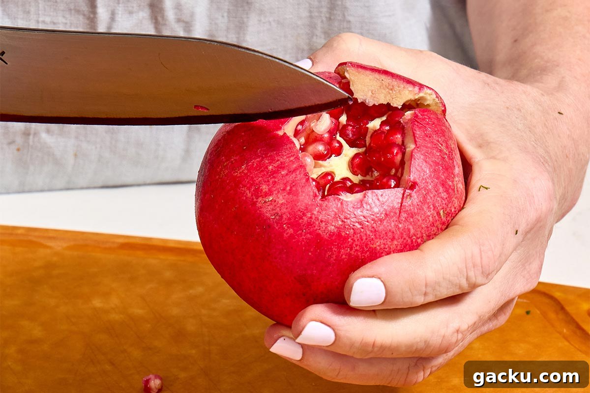 Woman slicing fresh pomegranate open with knife.