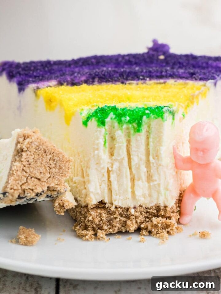 Close up of a slice of Mardi Gras cheesecake with a king cake baby on the side.