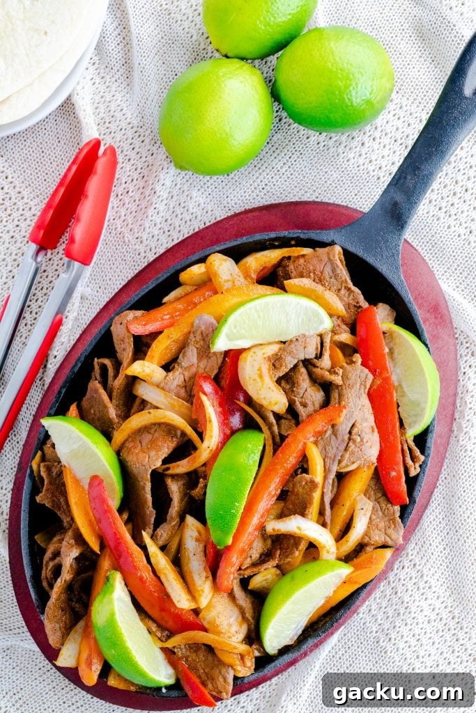 Steak fajitas in fajita skillet with red tongs and limes. 