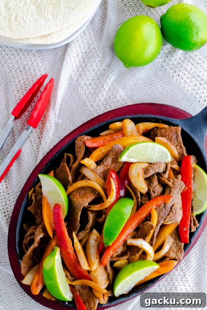Strips of steak, julienned red and orange peppers, with onions in fajita skillet with a side of tortillas. 