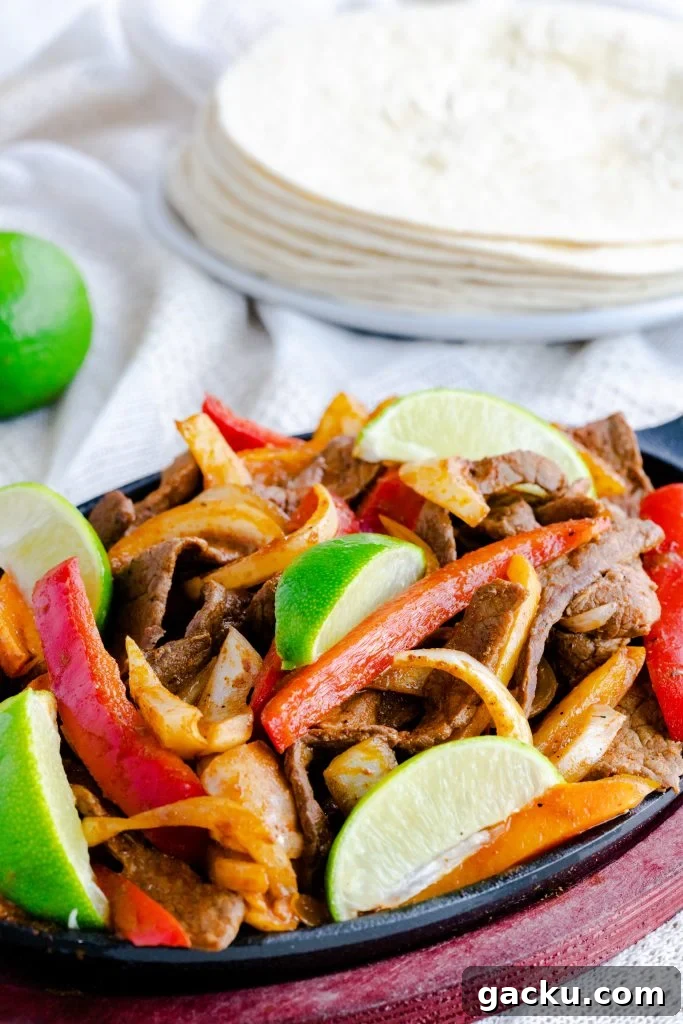Fajita skillet sitting on a wooden hot pad with sauteed onions and peppers, and steak.  