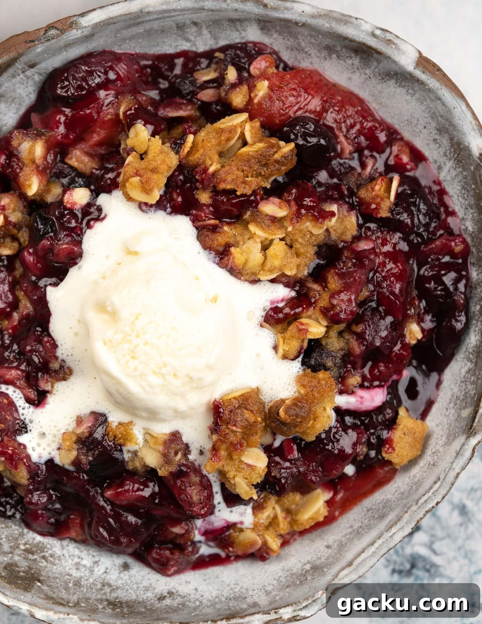 A scoop of vanilla ice cream on a bowl of berry crisp - crisp oatmeal topping on a gooey and jammy berry filling. 