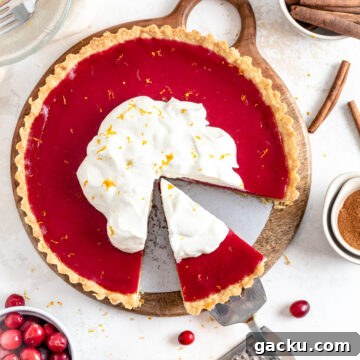 A cranberry tart with whipped cream, an orange and cinnamon sticks.