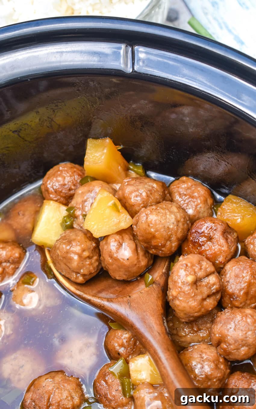 a wooden spoon scooping hawaiian meatballs out of a black crock
