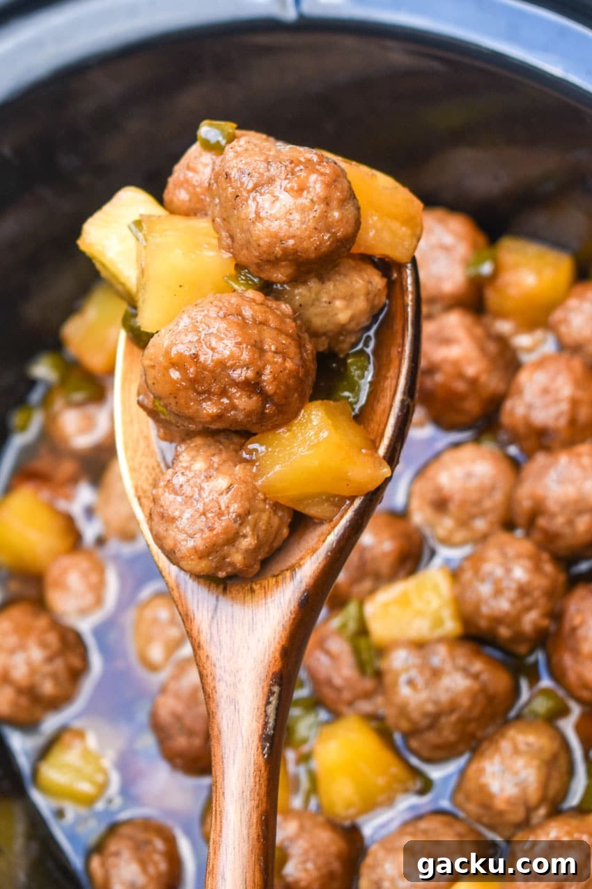 a wooden spoon holding up a scoop of crockpot hawaiian meatballs