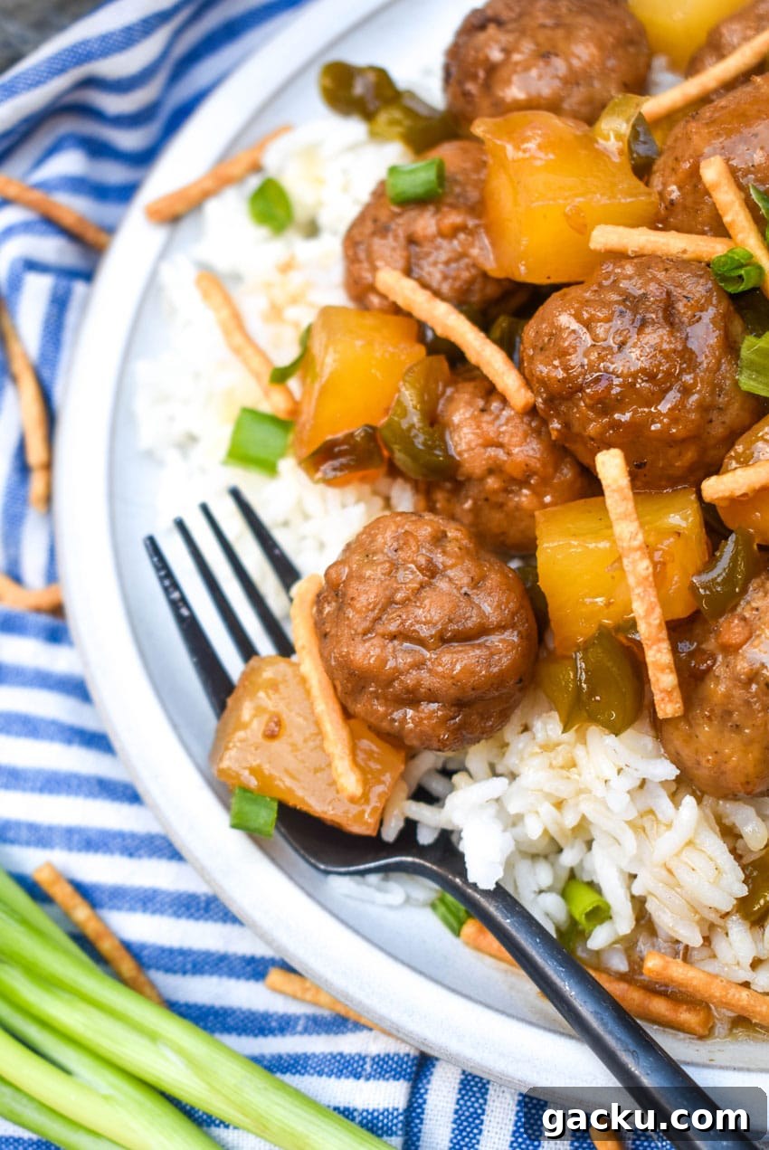 crockpot hawaiian meatballs over steamed white rice on a white dinner plate with a black fork resting on the side