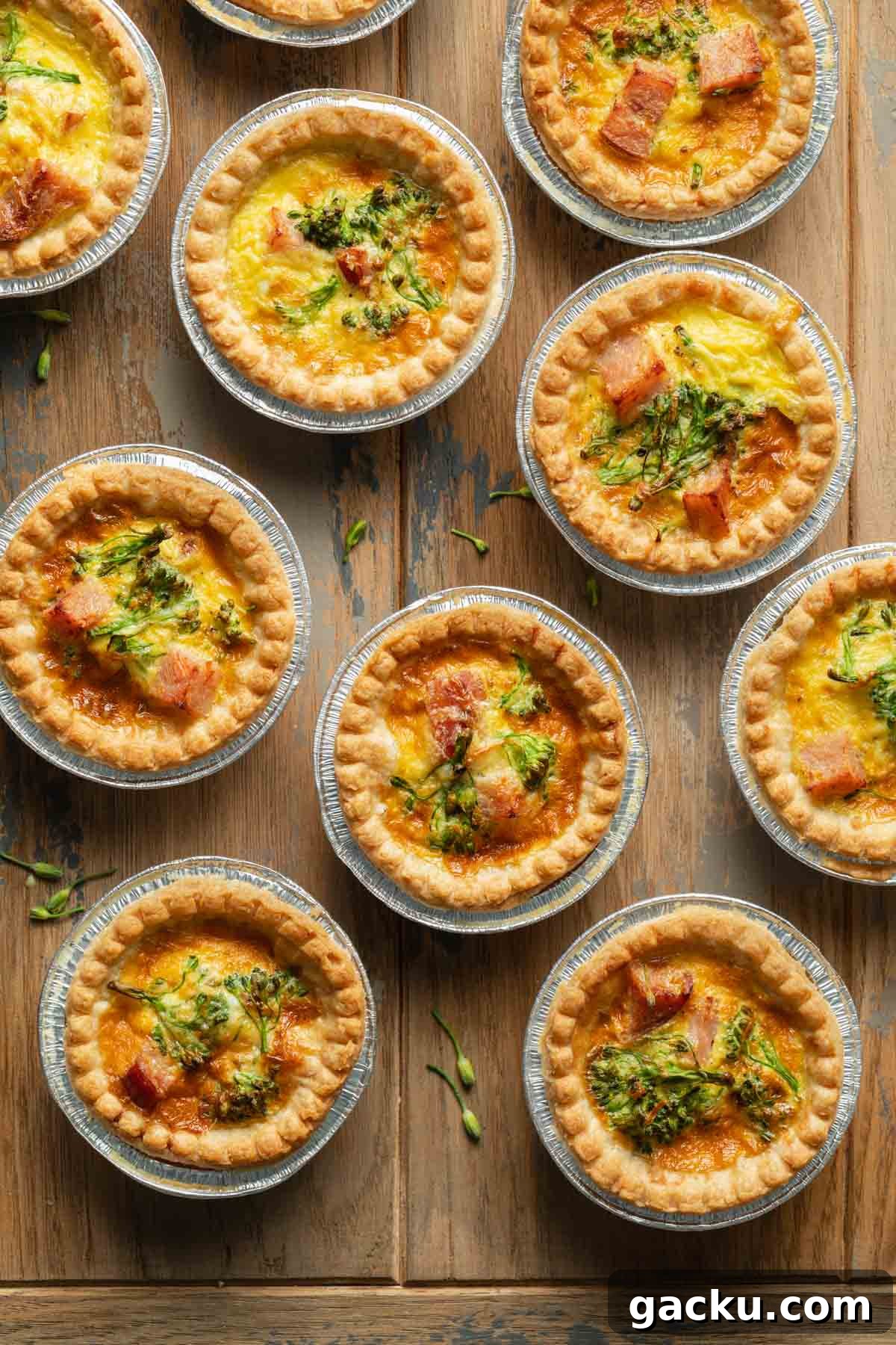 Mini quiches in foil tart shells arranged on a wooden surface.