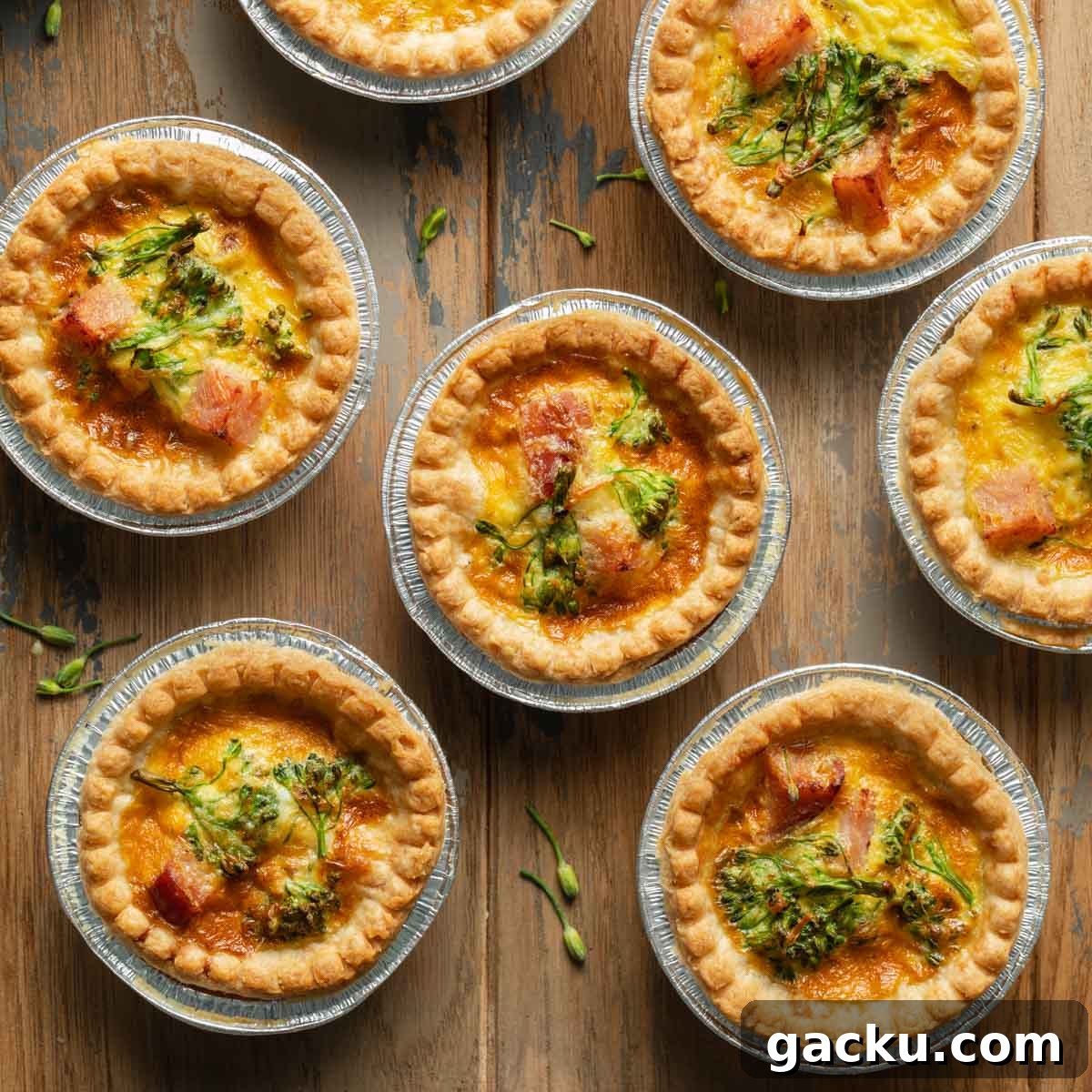 Mini quiche in tart shells arranged on a wooden surface.