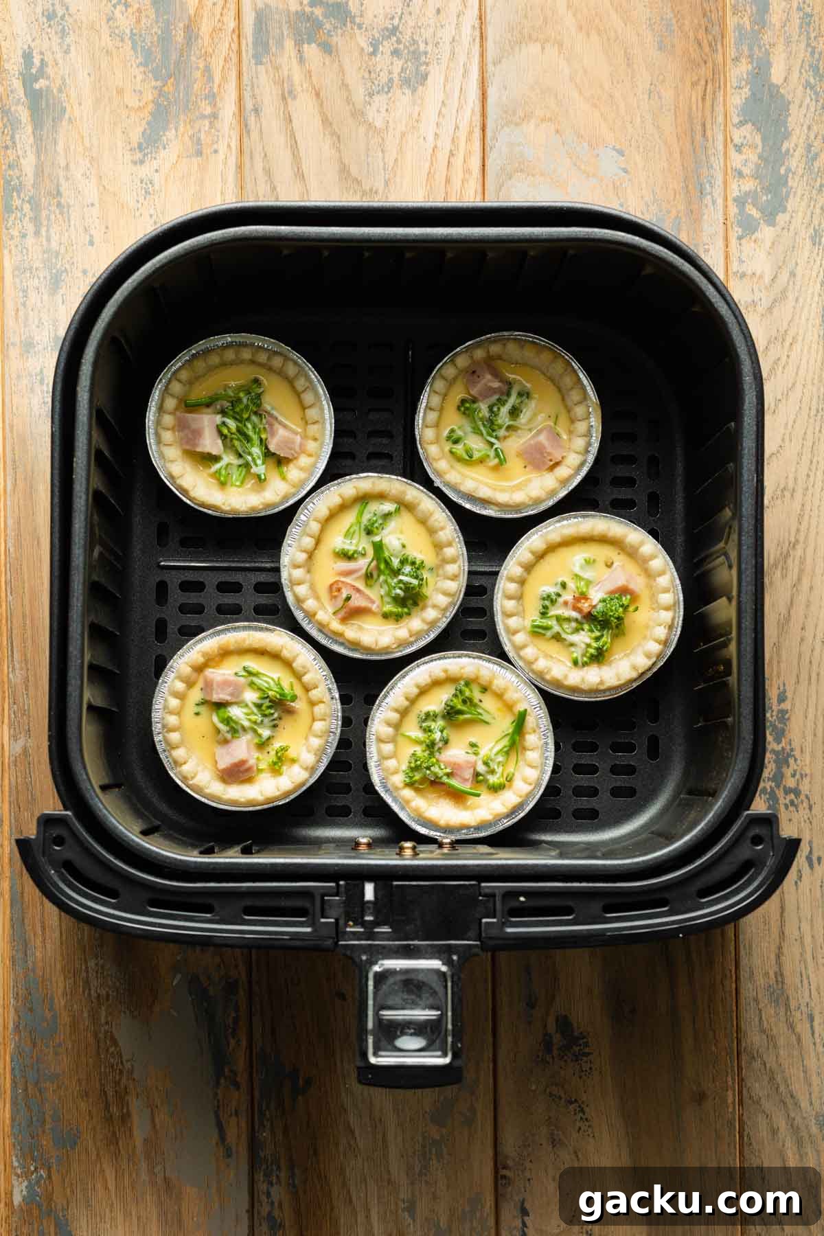 Par-baked tart shells filled with quiche filling in an air fryer basket.
