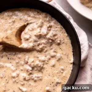 Southern-Style Sausage Gravy Recipe for Biscuits and Breakfast 6 A black cast iron pan with a sausage gravy and wooden spoon
