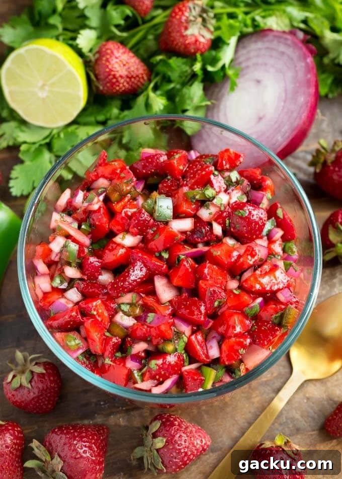 Fresh Strawberry Salsa in glass bowl next to herbs, fruit, and vegetables