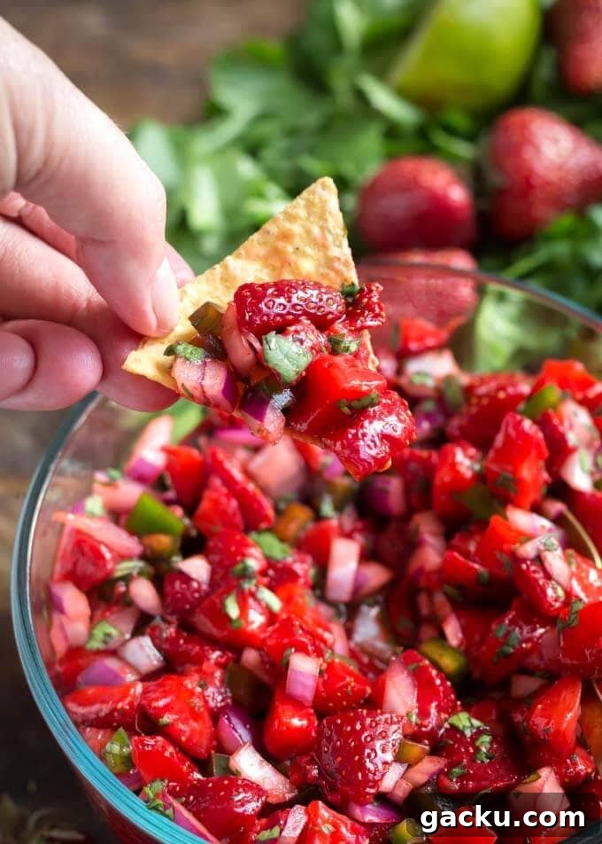Fresh Strawberry Salsa Recipe: Quick, Zesty Strawberry Salsa 3 hand using tortilla chip to scoop up Fresh Strawberry Salsa in glass bowl