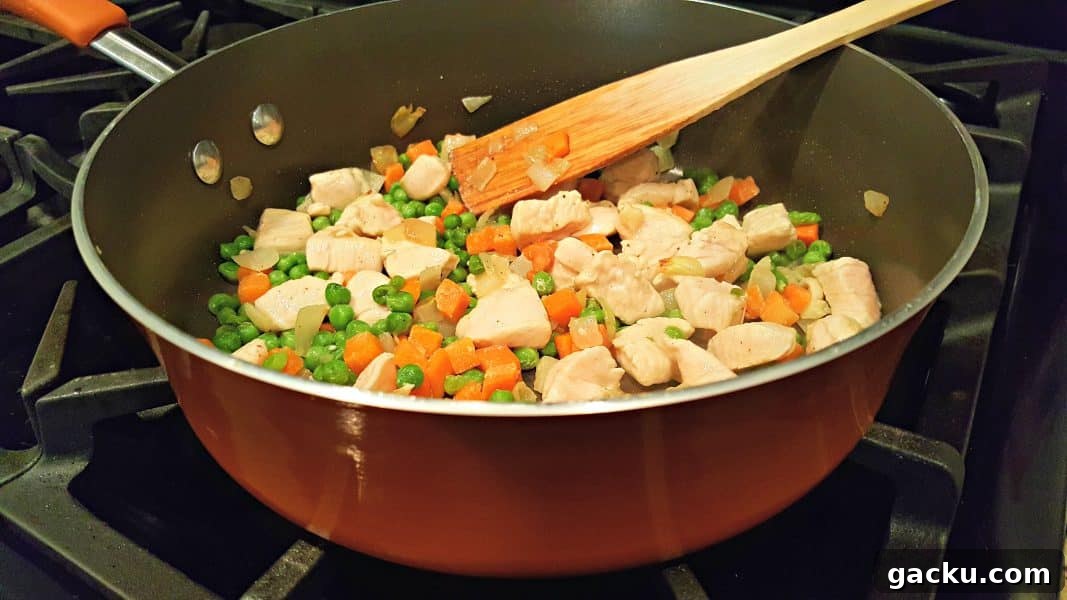 Ultimate Creamy Chicken Pot Pie Recipe for Comforting Weeknight Meals 3 chicken, peas, carrots and onions cooking in a pan.