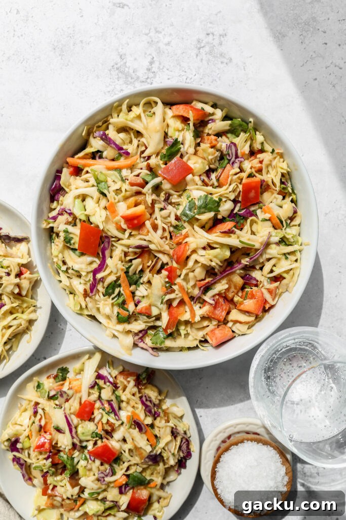 a white bowl of southwestern style coleslaw next to two white plates of slaw salad.
