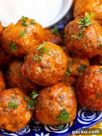 Close up of buffalo turkey meatballs garnished with fresh parsley on a small plate with a small dish of ranch.