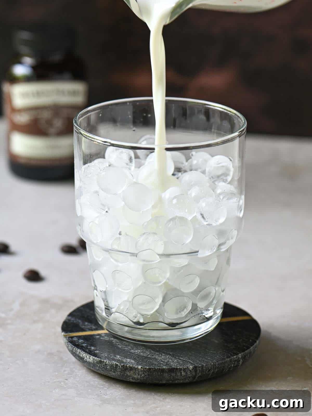 Milk being poured into a clear glass with ice.