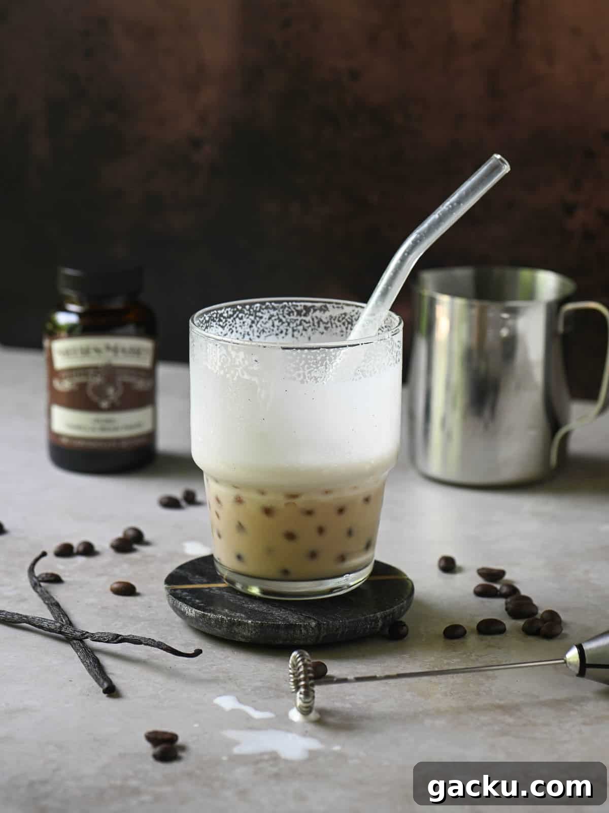 Eye-level view of a half-empty coffee latte in a clear cup on a beige surface.