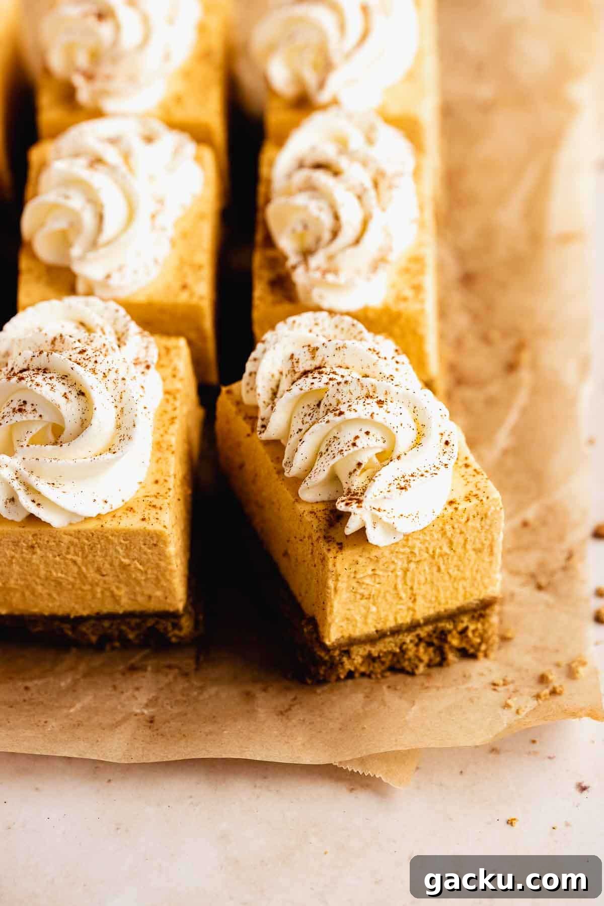 Pumpkin cheesecake bars with whipped cream on parchment paper