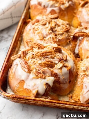 Baked carrot cake cinnamon roll with pecans and coconut on top in a metal pan on marble.