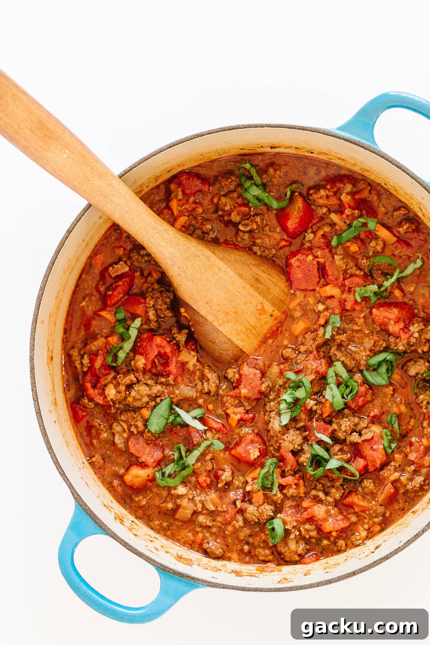 Authentic Bolognese Sauce Recipe for Rich, Slow-Simmered Pasta 2 Bolognese sauce in a dutch oven with blue handles and a wooden spoon sticking out