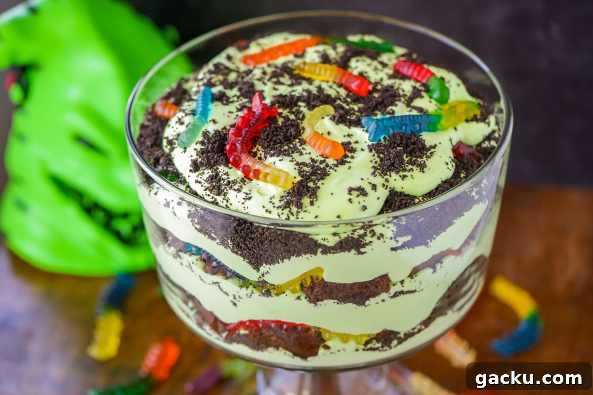 A spooky Oogie Boogie Trifle layered with chocolate cake, green mousse, crushed cookies and gummy bugs Oogie Boogie trifle close up image.