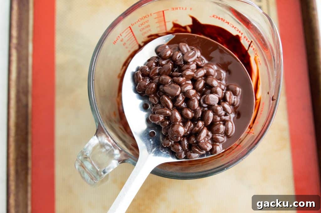 Chocolate covered espresso beans being scooped out of a measuring cup.