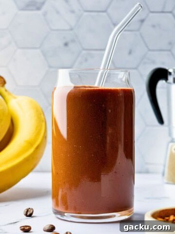 A glass filled with a chocolate smoothie with a glass straw in it.