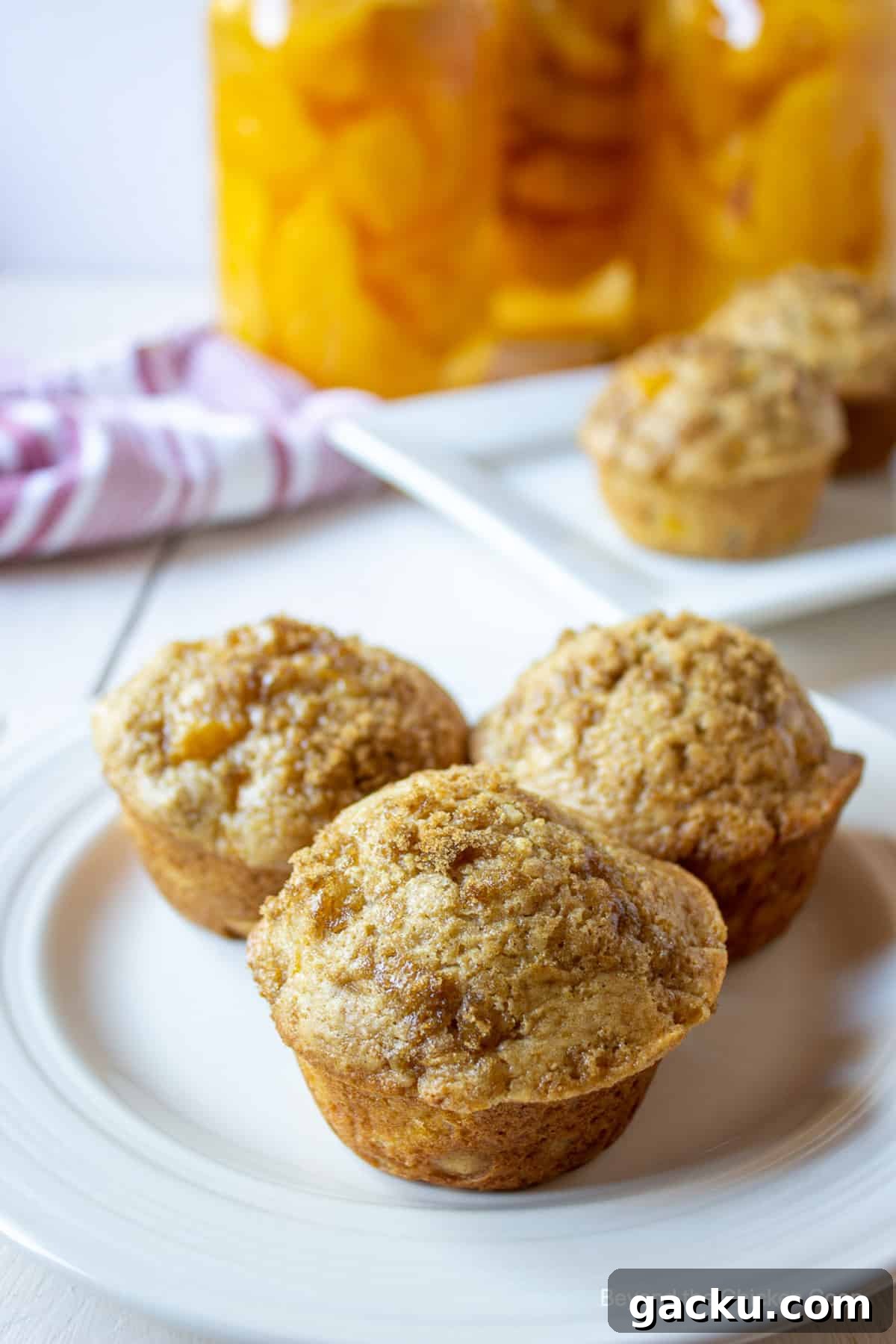 Juicy Peach Muffin Recipe for Perfect Summer Breakfast 11 Three muffins with a crumble topping on a white plate.