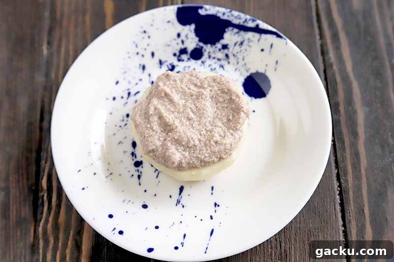 Horizontal oblique overhead image of a white plate with a blue pattern, topped with a slice of peeled pear spread with a ricotta and cinnamon mixture, on a brown wood table.