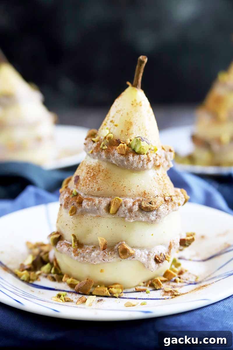 Vertical image of a pear and ricotta stack covered in chopped pistachios on a plate on a blue napkin.