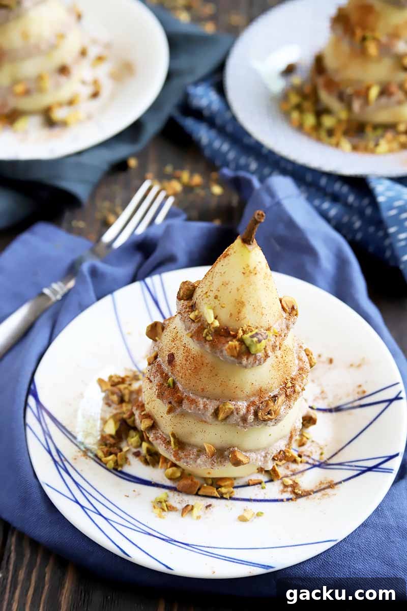 Vertical image of three plated desserts on blue napkins with stacked fruit slices and cream covered in pistachios.