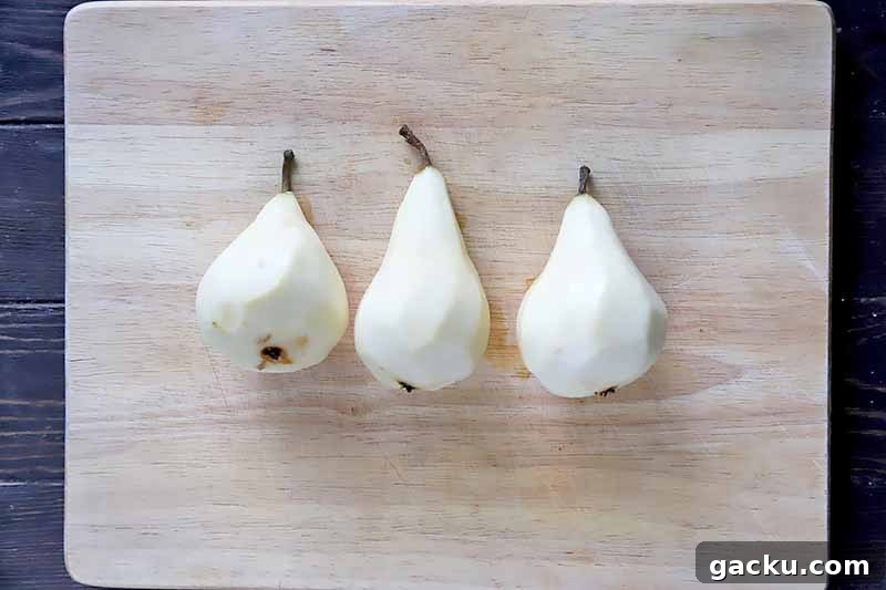 Horizontal image of three whole peeled pears on a wooden cutting board.