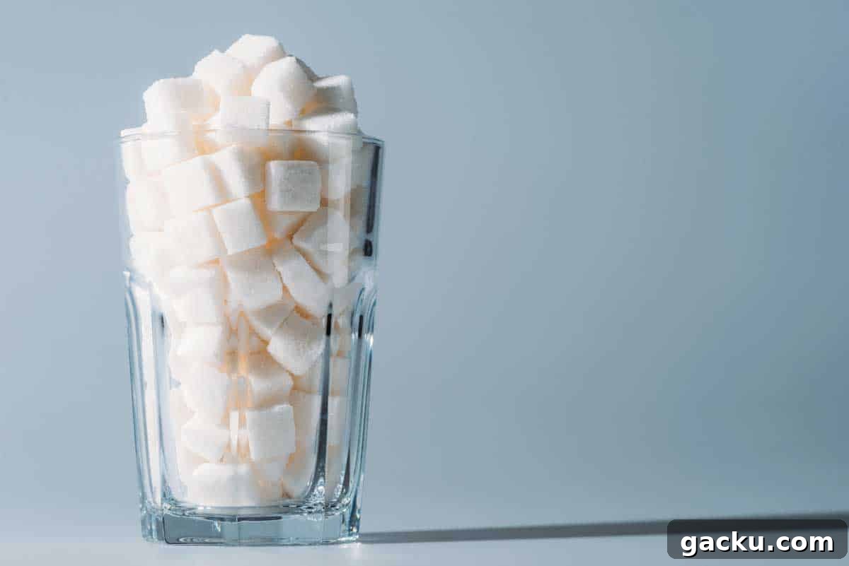 A glass full of white sugar cubes sits against a light blue background.