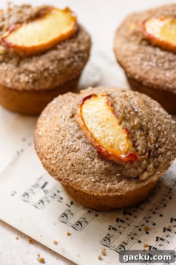 Homemade Peach Muffins with Fresh Summer Fruit 2 Three peach slices topped on bakery style muffins sitting on a sheet of music paper.