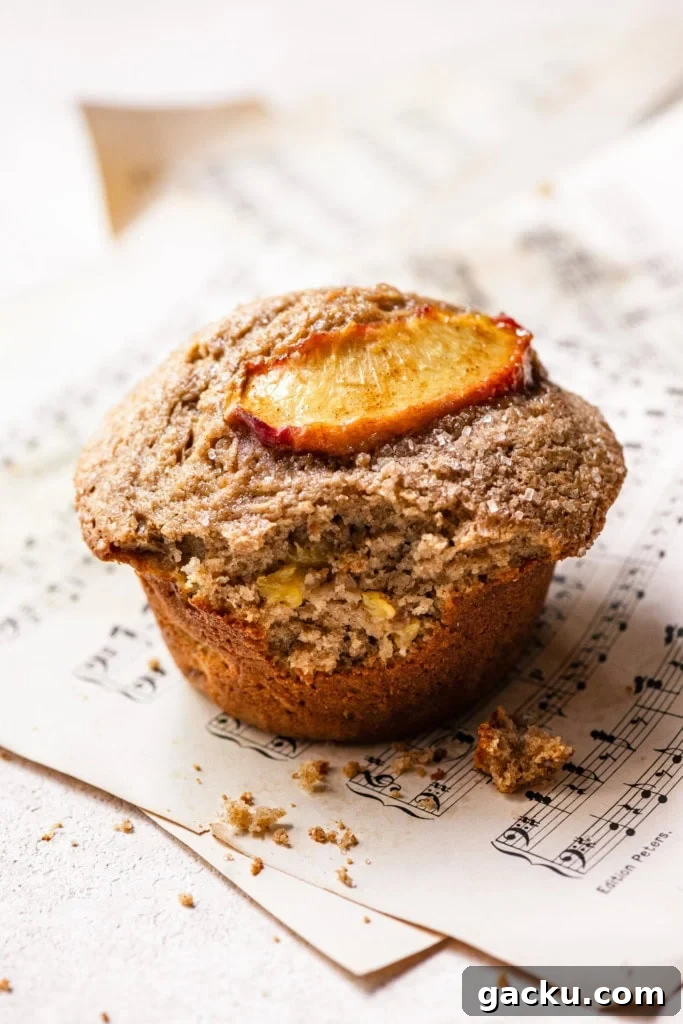 Homemade Peach Muffins with Fresh Summer Fruit 3 A single peach muffin with a large bite missing to show the inside full of peach chunks.