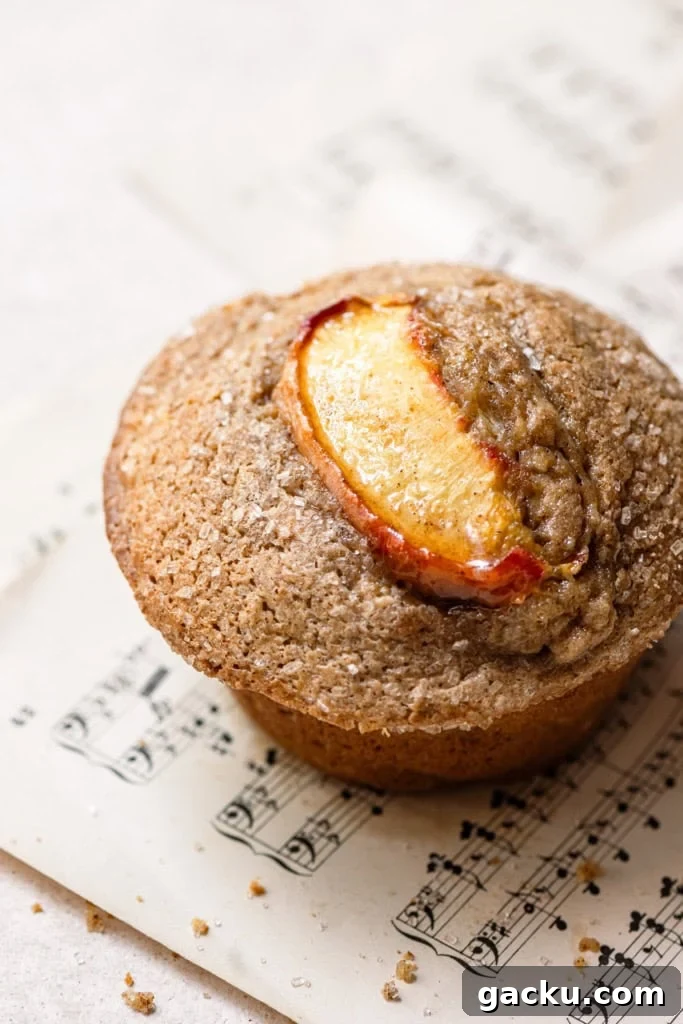 Homemade Peach Muffins with Fresh Summer Fruit 5 A muffin topped with peach slice and sugar sitting on a sheet of music paper.