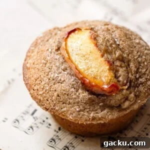Homemade Peach Muffins with Fresh Summer Fruit 10 Close up of a baked muffin topped with a peach slices on a sheet of music.