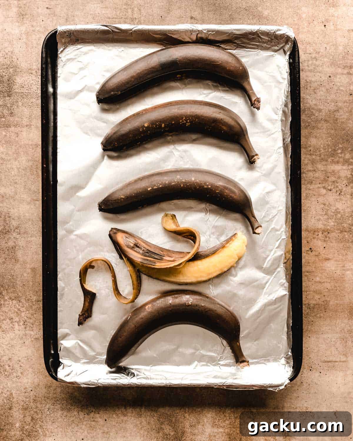 Brown bananas on a foil covered baking sheet with one banana peeled open.