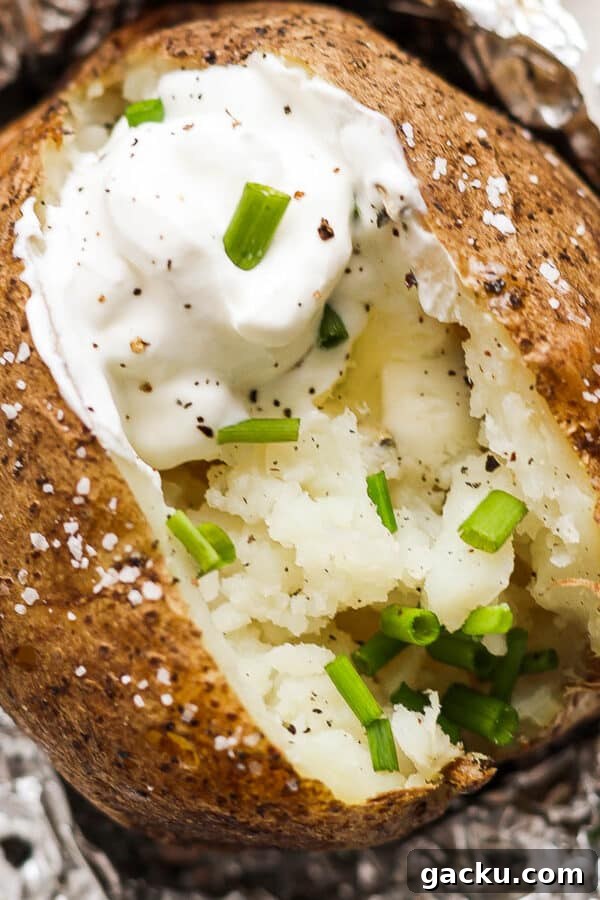 Smoked Potatoes Recipe: Crispy, Smoky Sides from the Grill 12 Top down shot of a grilled baked potato cut open with sour cream, butter, chives and pepper.