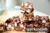 The Best S'more Fudge on brown parchment paper partially cut with two pieces of fudge stacked on top.