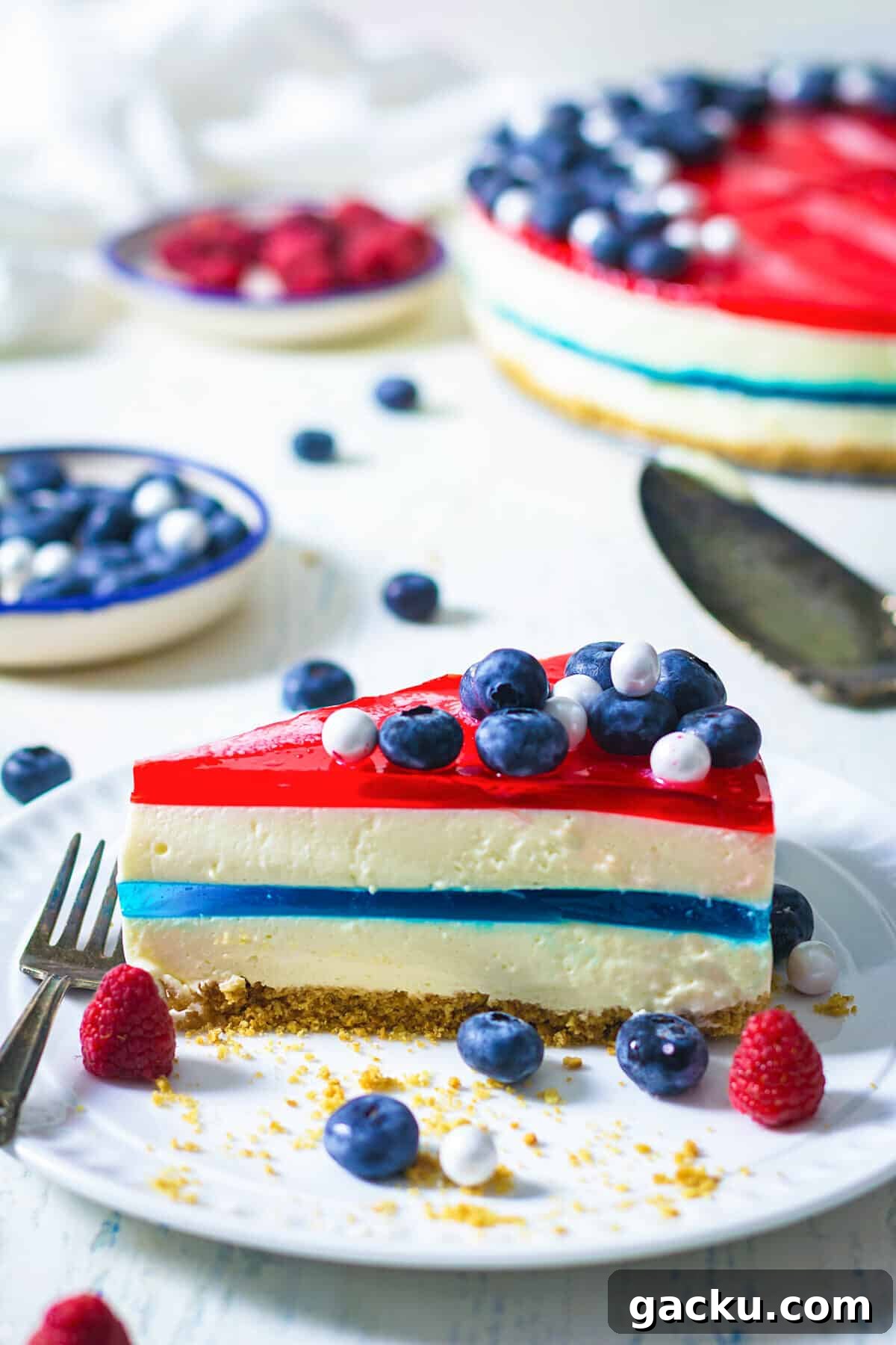 A slice of red white and blue jello on a white plate being served.