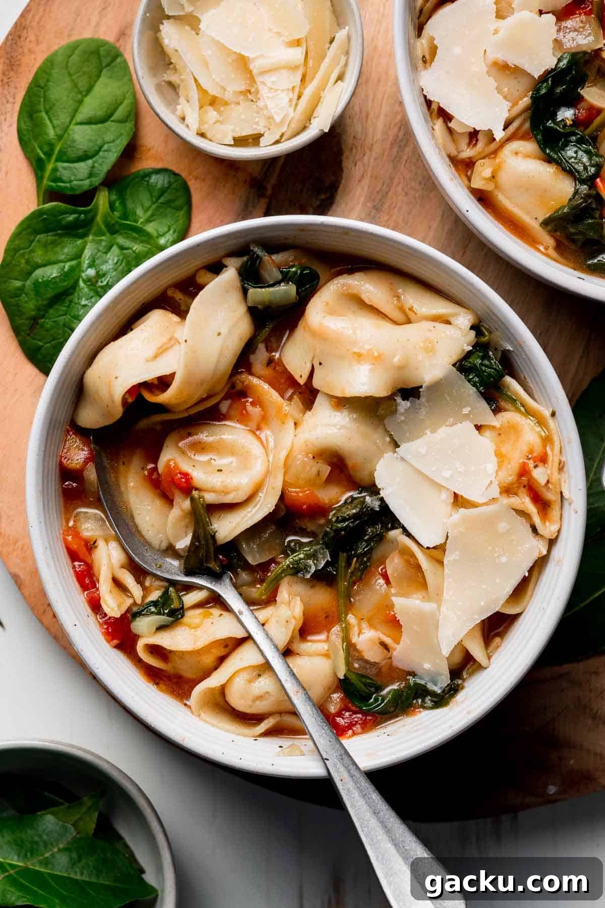 A bowl with tortellini and wilted spinach in a tomato broth garnished with parmesan cheese.